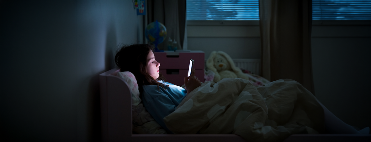 A child using a smartphone lying in bed in the dark
