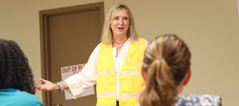 University at Albany’s Amy Nitza wearing a yellow high-vis vest and smiling addresses a participants at the start of the first full-scale immersive exercise of the Disaster Mental Health Training Program