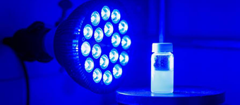 A lamp with over a dozen small blue bulbs shines at vial of light blue liquid
