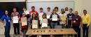 Thirteen high school students show off their certificates from robotics camp with their instructors on the right standing behind a table display the Petoi Robot Dogs they learned to program