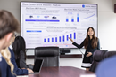 Student presenter gestures toward a screen displaying a data center industry analysis during a business presentation, while audience members listen from a conference table