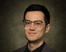 Professional headshot of assistant professor Jintao Zhang wearing dark-framed glasses and a dark collared shirt, photographed against a dark, neutral studio background