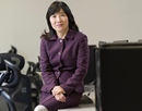 Professor Nancy Guo in purple suit sitting on a desk in an office