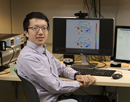 Professor Ziang Zhang wearing glasses seated at a desk in a research lab, with computer monitors displaying scientific data and diagrams