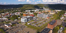 Aerial view of a campus complex featuring several academic and research buildings surrounded by parking lots, roads, and a residential neighborhood, with rolling hills in the distance