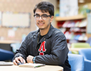 Image of Undergraduate student Mark Cortez in a letterman black jacket sitting at a table