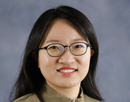 Professional headshot of a person wearing glasses against a gray studio background