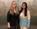 From left students Camilla Piano and Shreya Dhital standing side by side indoors in front of a textured wall, posing for a photograph