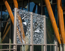 Decorative black-and-white mural panels are mounted on the exterior of a modern building, framed by large timber support beams and glass walls