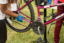 Close-up of a person wearing a blue glove adjusting the chain on a pink bicycle mounted on a repair stand outdoors