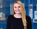 Professional headshot of assistant professor Katie Matt wearing a black top, standing in front of blue display cases
