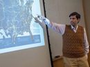 Presenter pointing to a map displayed on a projection screen during a lecture or presentation