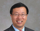 Professional headshot of distinguished professor Minghua Zhang wearing glasses, a dark pinstripe suit jacket, a light blue dress shirt, and a red tie against a plain gray studio background