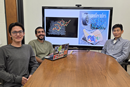 Three researchers sit around a conference table in a meeting room with computer monitors displaying research images and data