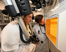 SUNY Suffolk student Arin Morton (left) simulates operating equipment in a hot cell facility — a specialized lab and equipment needed for processing radioactive materials — alongside mentor Michael Chimes of Brookhaven's Isotope Research & Production Department