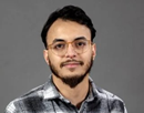 Headshot of assistant professor Walid Redjem from University of Albany in a checked shirt with a gray background