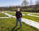 Assistant Professor of Ecosystem Science Amber Churchill standing in a grassy research field with multiple covered test plots arranged in rows behind them at the site of her experiment, located in Nuthatch Hollow