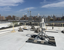 Rooftop weather monitoring equipment installed on a flat white roof, with city buildings visible in the background – a mesonet site