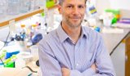 University at Buffalo’s professor Derek Daniels in front of a table with lab equipment