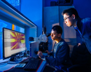 Huamin Li, associate professor of electrical and computer engineering, stands behind a student working on a computer at a desk.