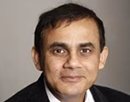 Professional headshot of professor Raj Sharman wearing a dark suit jacket, white dress shirt, and patterned tie against a plain light-colored studio background