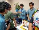 Students demonstrate STEM technology at a table display, explaining equipment and materials to visitors during a hands-on learning event