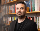 University at Buffalo’s associate professor Yotam Ophir dressed in black in front of a bookshelf