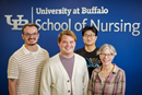Three people stand in front of a blue backdrop displaying the text “University at Buffalo School of Nursing.” The individuals are posed side by side for a group photo, wearing casual and business-casual clothing. The backdrop features the University at Buffalo logo and School of Nursing branding