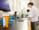 A prescription bottle in the foreground, pharmacy students working in the background