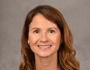 Professional headshot of professor Jana Shaw wearing a sleeveless dark navy top against a neutral gray studio background