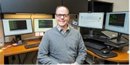 Upstate Medical University associate professor Jason Carbone in front of a desk with monitors