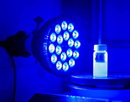 A lamp with over a dozen small blue bulbs shines at vial of light blue liquid