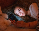 A teen girl lying in bed at night and using smartphone